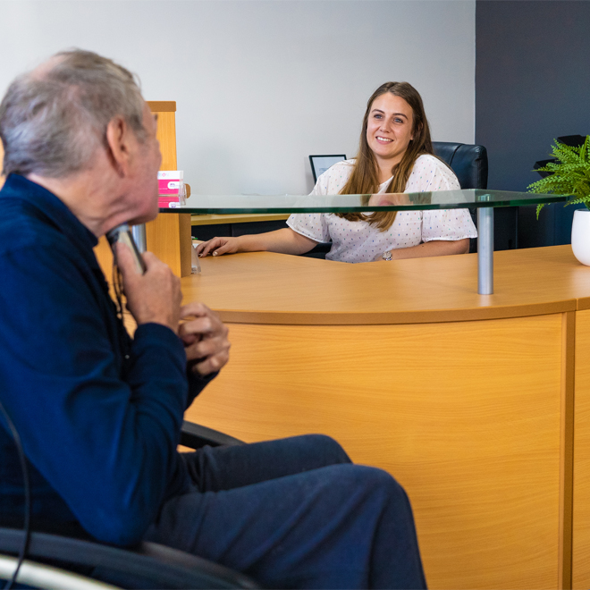 Elderly man in wheelchair at reception desk talking to receptionist