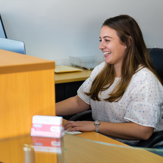 Reception staff sitting at computer desk smiling